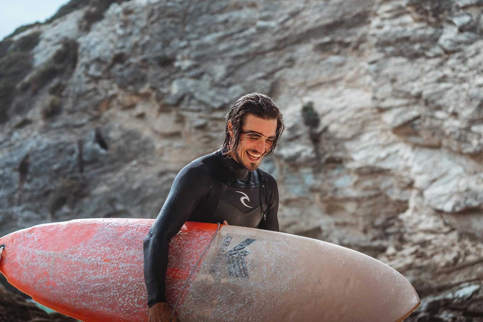 Surf en Portugal: Surfista con un traje de neopreno llevando una tabla de surf.